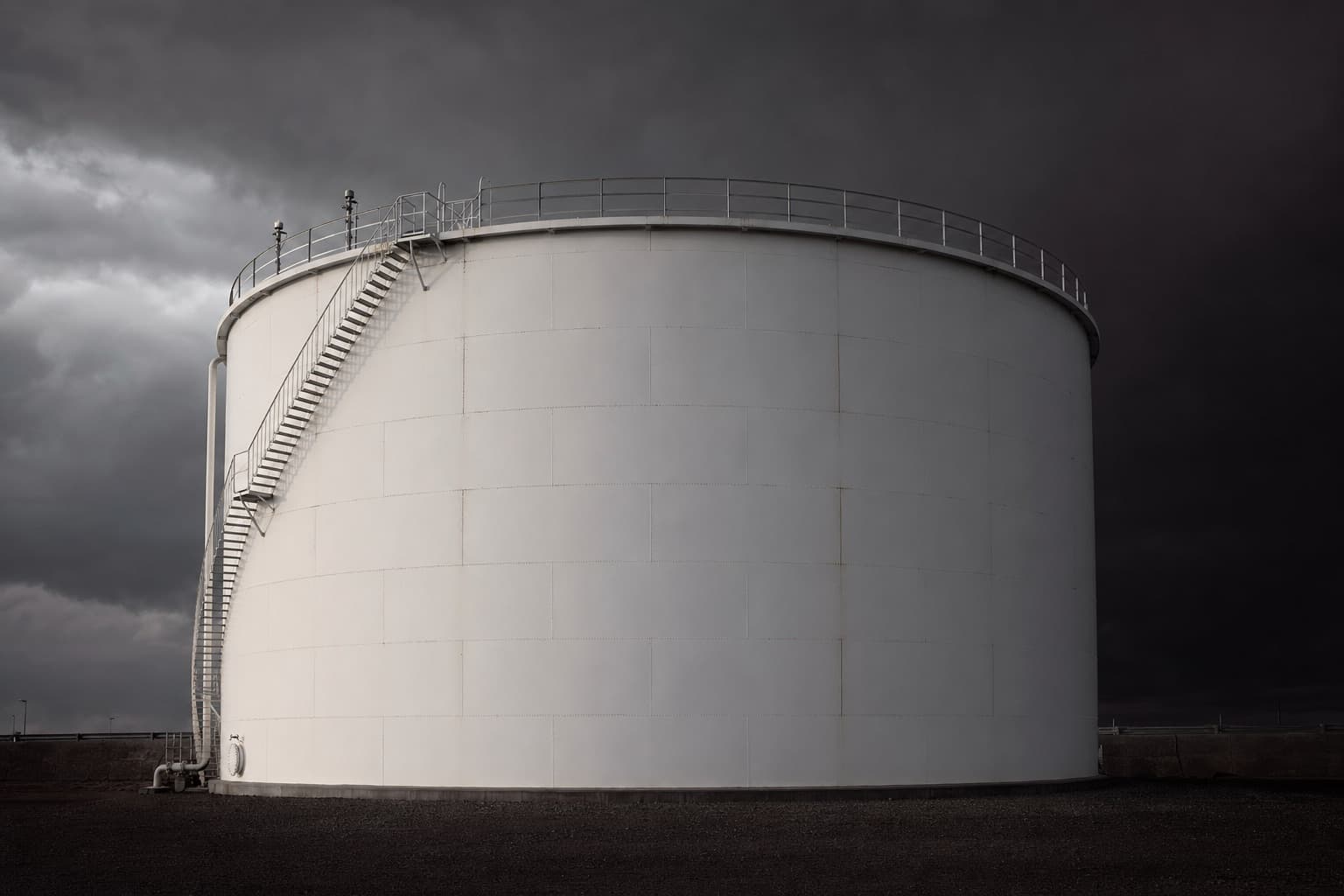 A large white cylindrical aboveground steel storage tank in service, seen from ground level