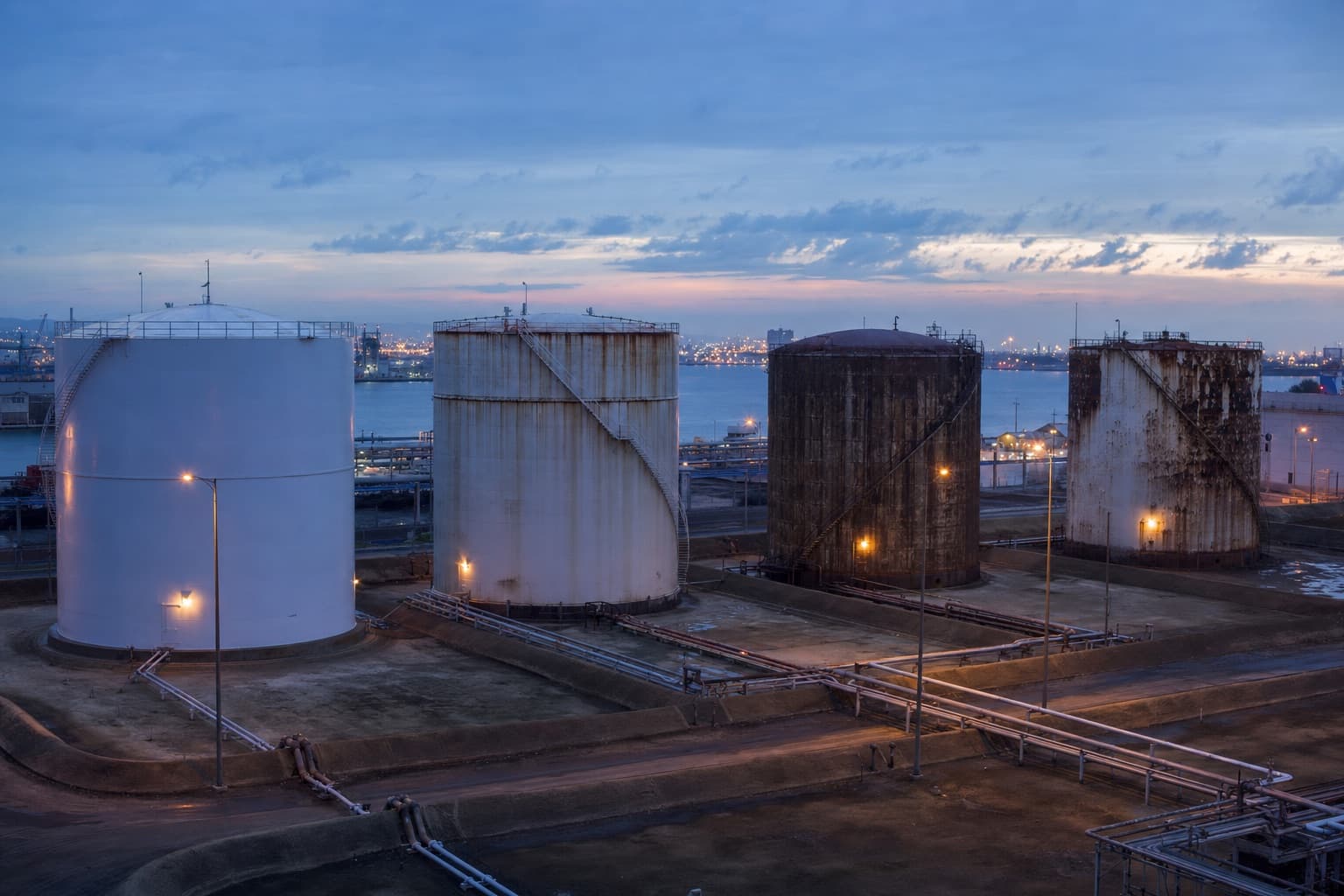 A tank farm at dusk, four tanks of different ages and coating conditions side by side